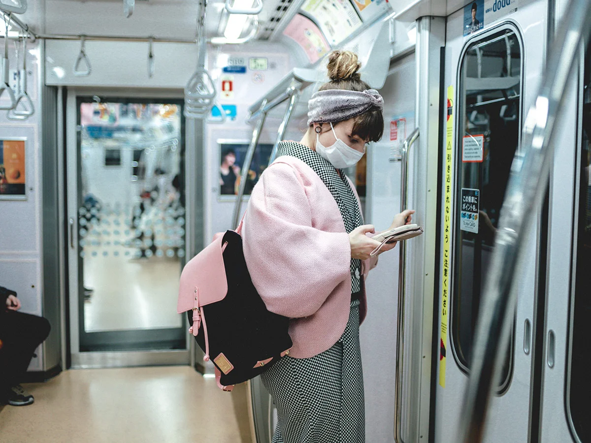 スターシャがマスクとバックパックCLÄSSY で電車に乗車中。立って携帯を見ている